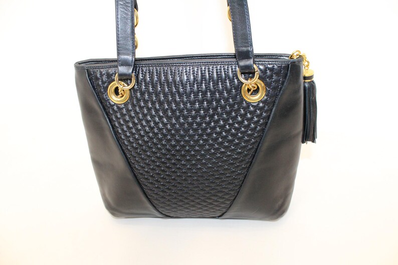May include: Black leather tote bag with gold-tone hardware. The bag features a quilted center panel and smooth side panels. Includes a tassel zipper pull and double shoulder straps.