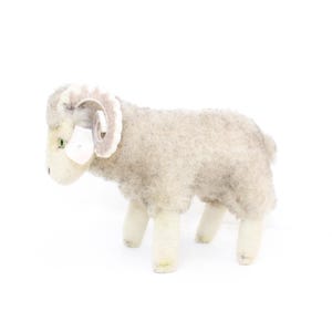 May include: A plush toy ram with white fur and brown horns. The ram has a white face with green eyes and a pink nose.