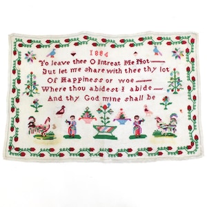 以下が含まれることがあります： 1884年のヴィンテージ刺繍サンプル。白い生地には赤と緑の花柄の縁取りが施されています。「To leave thee O Intreat Me Not...」などの刺繍テキストと装飾的な図形が特徴です。