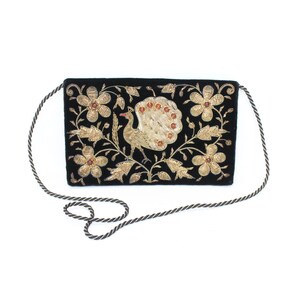 Pode incluir: Bolsa de mão retangular preta com um pavão bordado a ouro e um design floral. A bolsa tem uma alça longa e fina de corda. As penas da cauda do pavão são adornadas com pequenas contas vermelhas. As flores e folhas são douradas.