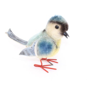 May include: A blue and yellow plush bird with red wire legs. The bird has a black beak and black eyes.