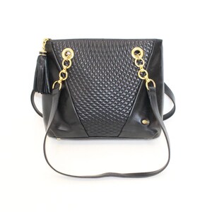May include: Black leather shoulder bag with gold-tone chain straps and a decorative tassel. The bag features a textured center panel and a rectangular shape. The bag has a long strap for shoulder or crossbody wear.