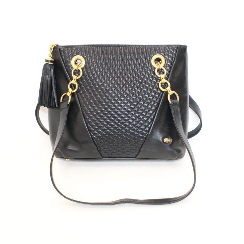 May include: Black leather shoulder bag with gold-tone chain straps and a decorative tassel. The bag features a textured center panel and a rectangular shape. The bag has a long strap for shoulder or crossbody wear.