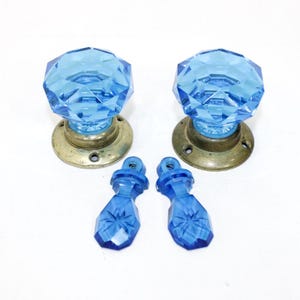 May include: Two blue faceted glass door knobs with brass bases and two matching blue glass pulls. The knobs have a diamond-like pattern. The hardware is likely for a cabinet or drawer.