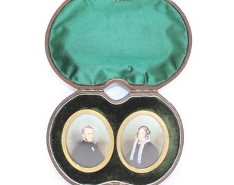May include: A wooden box with a green velvet interior, containing two oval-shaped portraits of a man and a woman. The portraits are framed in gold.