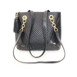 May include: Black leather tote bag with gold-tone chain accents and a tassel. The bag features a quilted center panel and two shoulder straps. The bag has a rectangular shape and a small gold logo.
