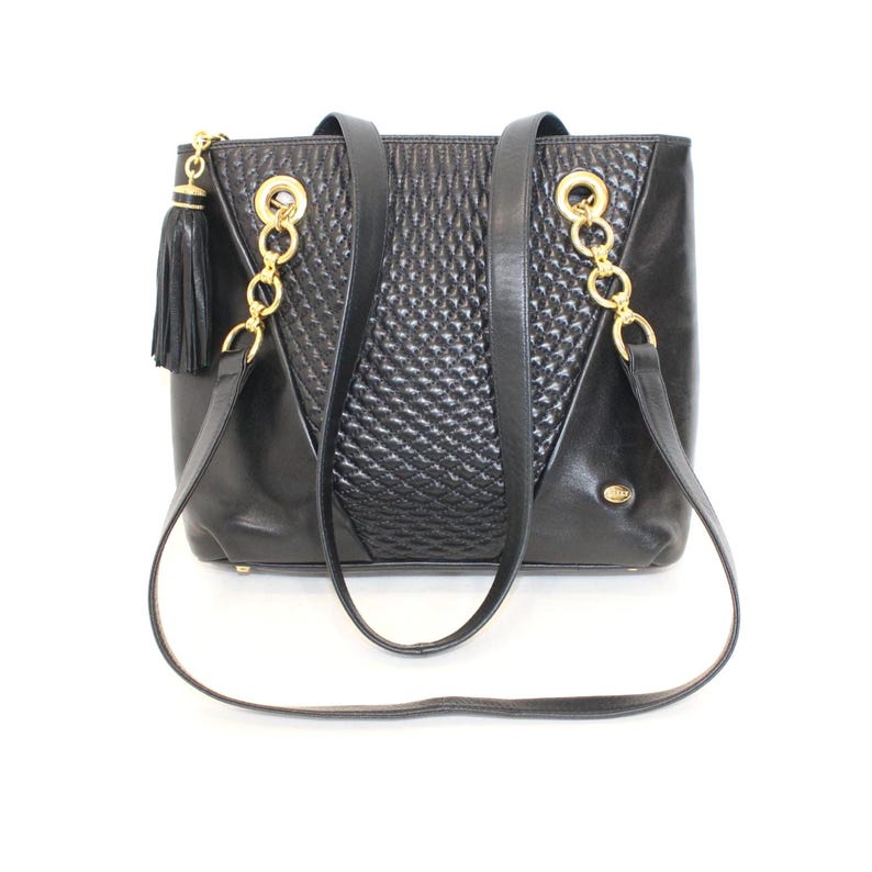 May include: Black leather tote bag with gold-tone chain accents and a tassel. The bag features a quilted center panel and two shoulder straps. The bag has a rectangular shape and a small gold logo.