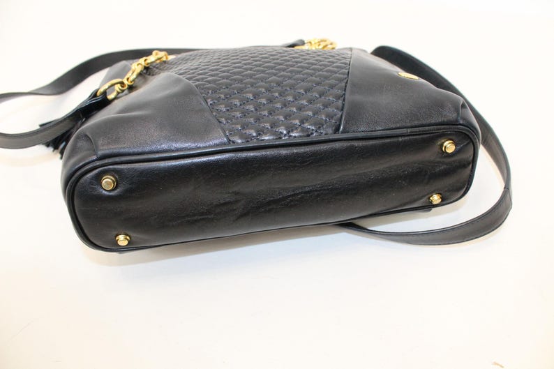 May include: Black leather shoulder bag with a quilted center panel and gold-tone chain and hardware. The bag has a long shoulder strap and a tassel detail. The bottom of the bag has four gold-tone feet.