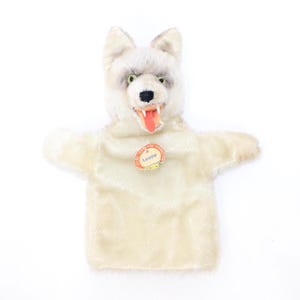 May include: A white and gray wolf hand puppet with a red tongue and green eyes. The puppet has a tag that says "Loopy". The puppet is made of a soft, plush material.