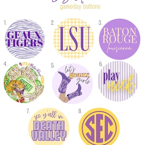 May include: A collection of eight round buttons with purple and gold designs. The buttons feature text like "GEAUX TIGERS," "LSU," "Baton Rouge," and "SEC." Some buttons have patterned backgrounds, including stripes and gingham.
