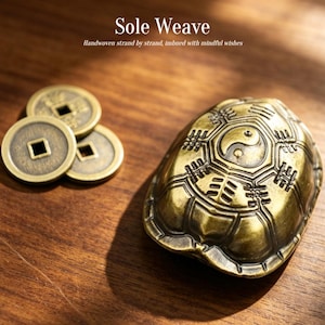May include: A brass-colored metal turtle figurine featuring a yin-yang symbol and geometric patterns on its shell, accompanied by three round brass-colored coins with square center holes. The text "Sole Weave" and "Handwoven strand by strand, imbued with mindful wishes" is visible.