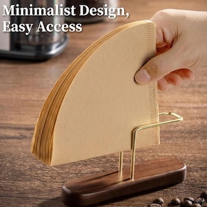 Può includere: Un portafiltro per caffè con base in legno e supporto in metallo dorato. Il supporto è pieno di filtri di carta marrone. Il testo "Minimalist Design, Easy Access" è visibile.