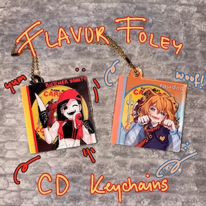 May include: Two CD keychains with cartoon illustrations. One features a character in a red outfit holding a knife and meat, with the text "BUTCHER VANITY". The other shows a dog-like character with the text "rawdog". The keychains have gold-colored chains and the text "FLAVOR FOLEY" and "CD Keychains".