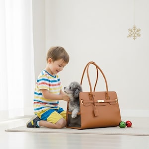 Op de afbeelding: Een bruinleren draagtas voor huisdieren met een kleine grijze hond erin. De tas heeft twee handvatten en een rechthoekige vorm. Een kind knielt naast de tas en aait de hond. Twee kerstballen liggen op de grond.