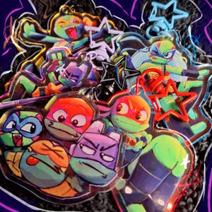 May include: A collection of colorful Teenage Mutant Ninja Turtles character stickers. The stickers feature the turtles in various action poses, with vibrant green, orange, blue, and purple masks. Star-shaped charms are also included in the design.