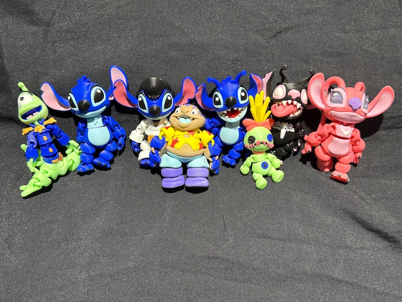 Puede incluir: Una colecci&oacute;n de figuras de personajes coloridos, que incluyen criaturas azules, verdes y rojas con orejas grandes y caras expresivas. Las figuras est&aacute;n dispuestas sobre una superficie gris oscuro.