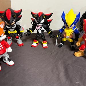 May include: Five action figures of popular characters. The figures include a red fox in a red hoodie, a black and grey figure, a black figure with white teeth and tongue, a blue and yellow figure, and a red figure with gold boots.