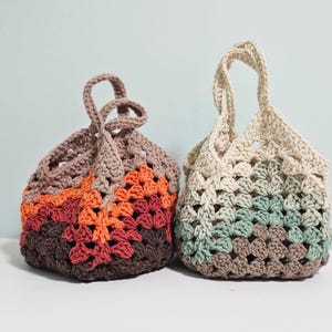May include: Two handmade crochet bags. The bag on the left features a color block design in shades of brown, orange, and red. The bag on the right has a cream, green, and brown color scheme. Both bags have handles.