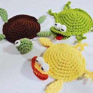 May include: Handmade crochet turtle and frog toys in brown, green, and yellow. The turtle has a brown shell and green flippers. The frog toys are green and yellow with white eyes and red tongues. These whimsical toys are perfect for children.