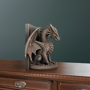 Op de afbeelding: Een bronzen drakenboekensteun. De draak zit met gespreide vleugels en is geplaatst tegen een donkergrijze rechthoekige steun. De draak heeft gedetailleerde schubben en een felle uitdrukking. De boekensteun staat op een houten oppervlak.