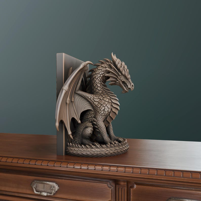 Op de afbeelding: Een bronzen drakenboekensteun. De draak zit met gespreide vleugels en is geplaatst tegen een donkergrijze rechthoekige steun. De draak heeft gedetailleerde schubben en een felle uitdrukking. De boekensteun staat op een houten oppervlak.