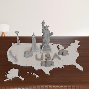May include: A gray 3D-printed map of the United States with miniature landmarks, including the Statue of Liberty, the Empire State Building, and the Space Needle. The word "USA" is spelled out in large letters on the map.