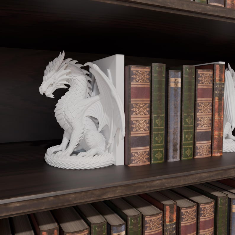 Op de afbeelding: Witte drakenboekensteunen op een donkere houten plank. De draak is gedetailleerd met vleugels en schubben. Boeken met verschillende gekleurde ruggen zijn tussen de boekensteunen geplaatst.