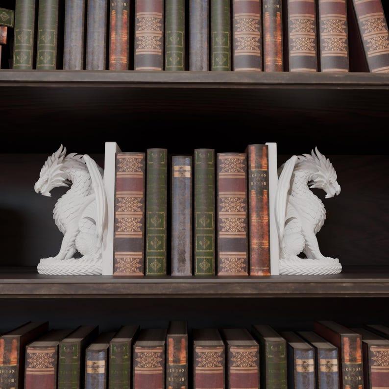 Op de afbeelding: Witte drakenboekensteunen met gedetailleerde vleugels en schubben, die een rij vintage boeken op een donkere houten plank flankeren. De boekensteunen voegen een vleugje fantasie toe aan elke boekenplank. De boeken hebben verschillende kleuren en texturen.