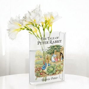 May include: A white ceramic mug with a black handle and the text "But First, Coffee" in a black, handwritten-style font. The mug is on a white surface.