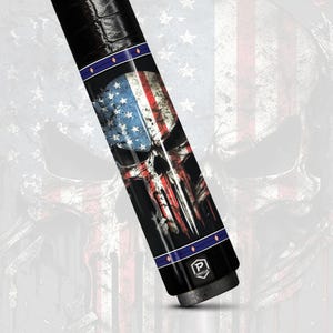 May include: A black pool cue with a skull graphic featuring the American flag design. The cue has a textured grip and blue and white accents. The skull graphic is red, white, and blue.