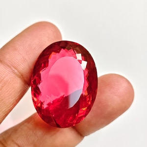 Può includere: Una gemma sfaccettata di forma ovale in un colore rosso profondo e saturo. La pietra presenta una superficie lucida con numerose sfaccettature geometriche che riflettono la luce, creando un aspetto brillante e traslucido con profondità.