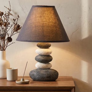 May include: A white ceramic mug with a black handle and the text "But First, Coffee" in a black, bold font. The mug is sitting on a white surface. The mug is approximately 4 inches tall.