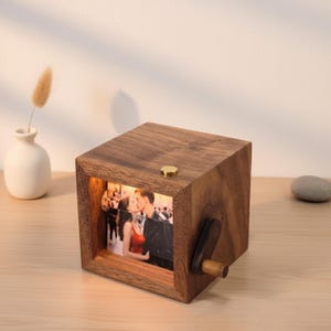 May include: A white ceramic mug with a black handle and the text "But First, Coffee" in a black, handwritten-style font. The mug is on a white surface.