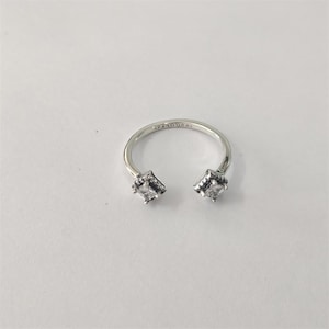 May include: A silver ring with a horseshoe design. The ring has two square, clear gemstones at the open ends. The word "PANDORA" is engraved on the band. The ring is set against a white background.