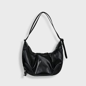 May include: Black shoulder bag with a curved, pleated design. It features a long, thin strap and a small decorative element. The bag is made of a smooth material and has a minimalist aesthetic. The bag's measurements are in centimetres.