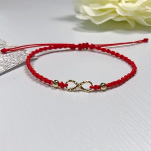 Op de afbeelding: Rood koord armband met een gouden oneindigheidsbedel en twee gouden kralen.