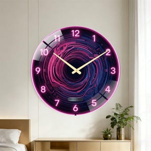 May include: A round wall clock with a neon pink and blue design. The clock face features a digital circuit board pattern and gold hands. The numbers are in a modern font. The clock is mounted on a light-colored wall.