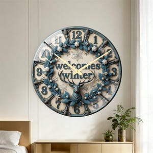 May include: A round wall clock with a blue and cream color scheme. The clock face features a deer, snowflakes, and the words "welcomes winter." The clock hands are gold.