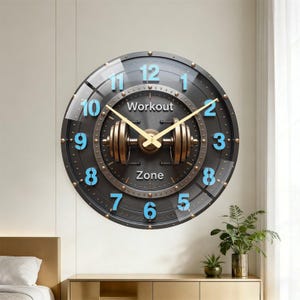 May include: A round wall clock with a dark metallic finish, featuring a central bronze-colored dumbbell graphic. The clock face displays light blue raised numerals from 1 to 12, with the text "Workout" above and "Zone" below the central dumbbell.