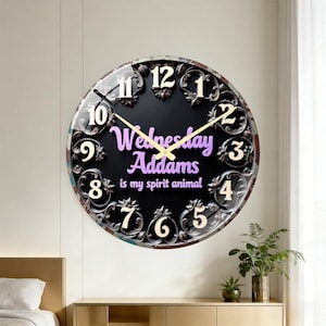 May include: A round wall clock with a black face, ornate dark scrollwork border, and cream-colored numerals. The center features the purple text "Wednesday Addams is my spirit animal" with thin gold clock hands pointing to the time.