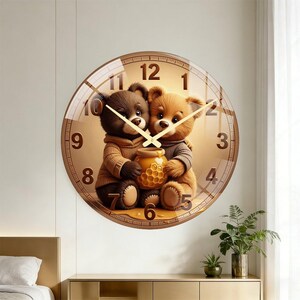 May include: A round wall clock featuring a graphic of two teddy bears, one dark brown and one light brown, sitting together and holding a honey pot. The clock face has large brown numerals from 1 to 12 and thin gold-coloured hour and minute hands.