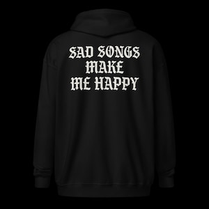 Peut inclure: Un sweat à capuche noir avec l'inscription blanche "SAD SONGS MAKE ME HAPPY" en police gothique dans le dos. Le sweat à capuche a une capuche et des manches longues. Le fond est noir.