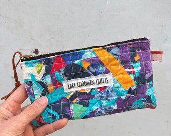 May include: A colorful patchwork zippered pouch with a label that reads "Kari Goodwin Quilts". The pouch is made from a variety of fabrics in shades of blue, purple, red, yellow, and green.