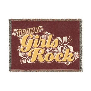 May include: A maroon woven throw blanket with the words "Trojan Girls Rock" in yellow script. White floral accents surround the text. The blanket has a fringed edge.