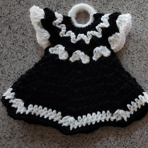 May include: A black and white crocheted dishcloth shaped like a dress with a ruffled neckline and a white loop at the top.
