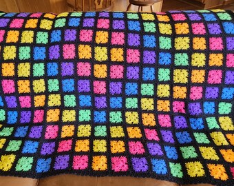 May include: A rainbow crochet blanket with black squares. The blanket is made with a variety of bright colors, including red, orange, yellow, green, blue, indigo, and violet.