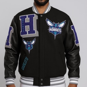 Pode incluir: Casaco universitário preto com mangas de couro, com o logotipo dos Charlotte Hornets e o emblema "H". O casaco tem detalhes em branco, cinza e azul, com o nome e o logotipo da equipa. Fecho de botões e punhos listrados.