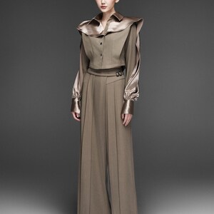 May include: A two-piece ensemble featuring a cropped, button-down top with a wide, satin collar and long sleeves. The top is paired with high-waisted, wide-leg trousers. The outfit is a muted brown color with a satin finish on the top.