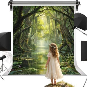 Peut inclure: Une personne vêtue d'une robe crème se tient devant une toile de fond représentant une scène de marais verdoyant avec une rivière et des arbres. Un équipement d'éclairage de studio, comprenant des boîtes à lumière et des parapluies, est installé.