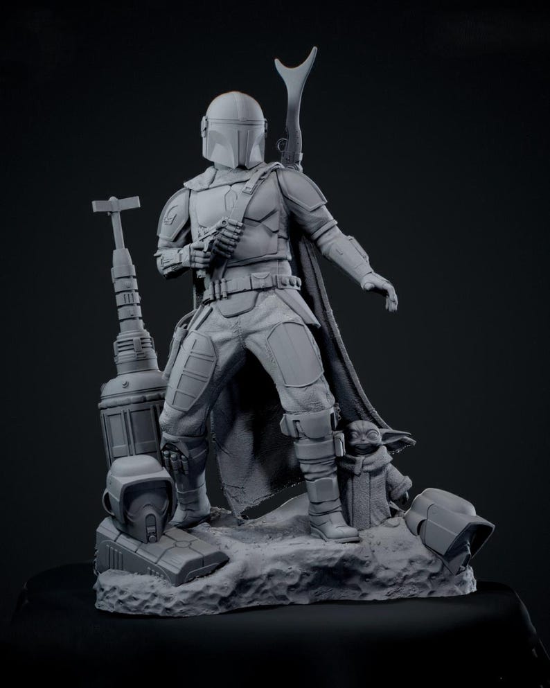 Puede incluir: Una figura gris de Mandaloriano con casco, armadura y capa, sosteniendo un arma. Una peque&ntilde;a figura de Grogu est&aacute; cerca. La base incluye un bl&aacute;ster, un casco y otros accesorios. La estatua es una representaci&oacute;n detallada.